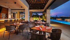 An outdoor dining area with wicker chairs and tables, a bar with bottles, and a pool in the background. - The Santa Maria, A Luxury Collection Hotel & Golf Resort, Panama City (Panama City)