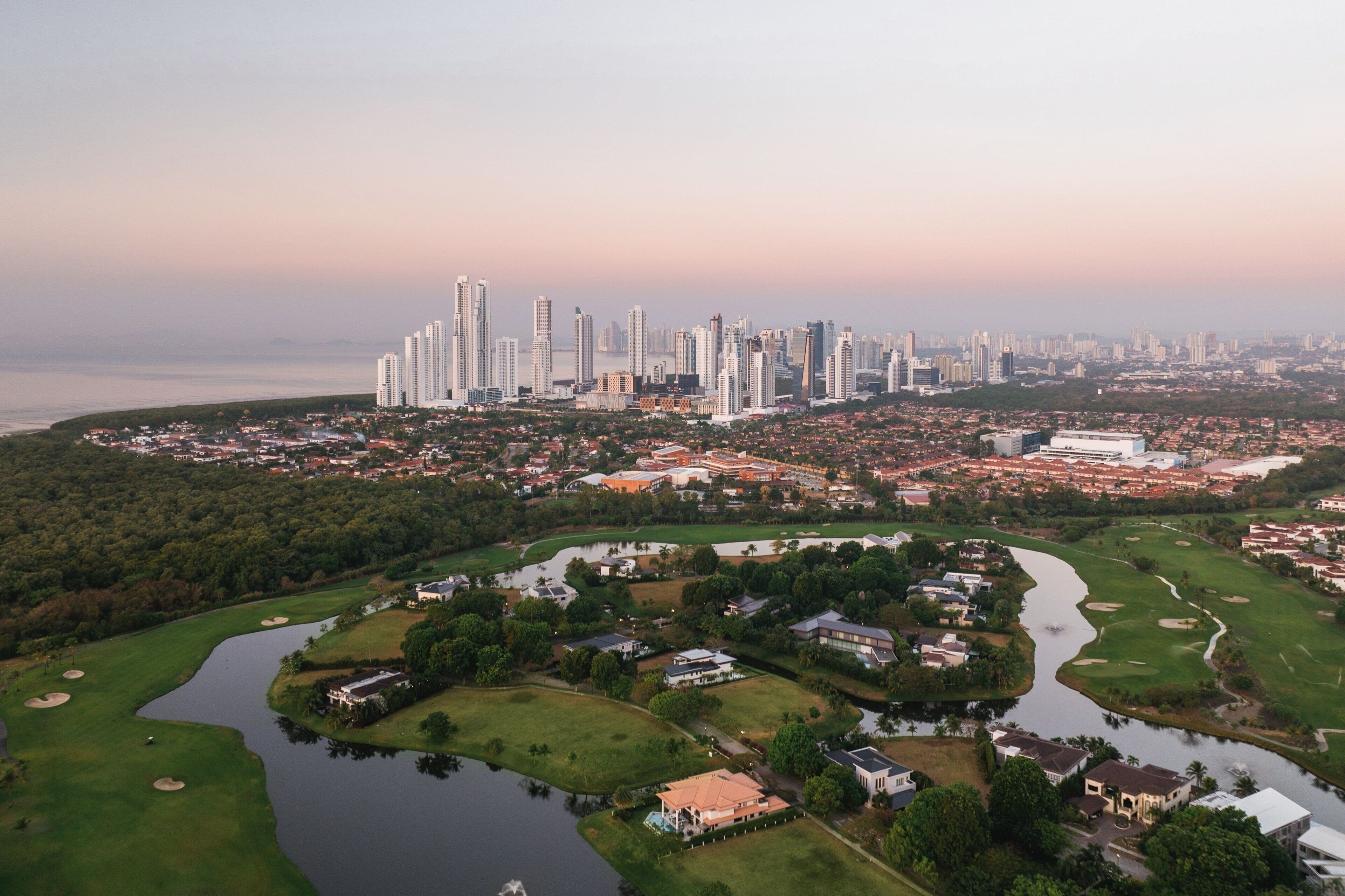Une vue aérienne d’une ville avec de hauts immeubles, un terrain de golf et une étendue d’eau.