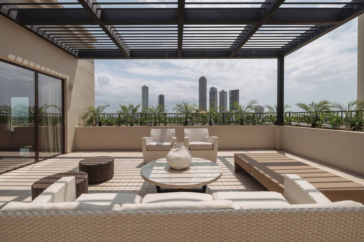 A rooftop terrace with outdoor seating, a view of city buildings, and a pergola structure.