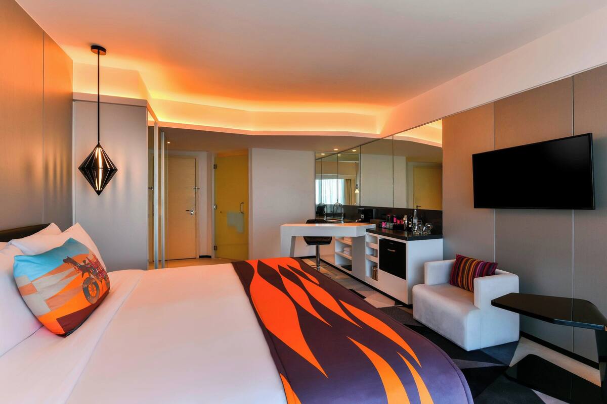 A modern hotel room with a bed, a sofa, a desk, and a TV.