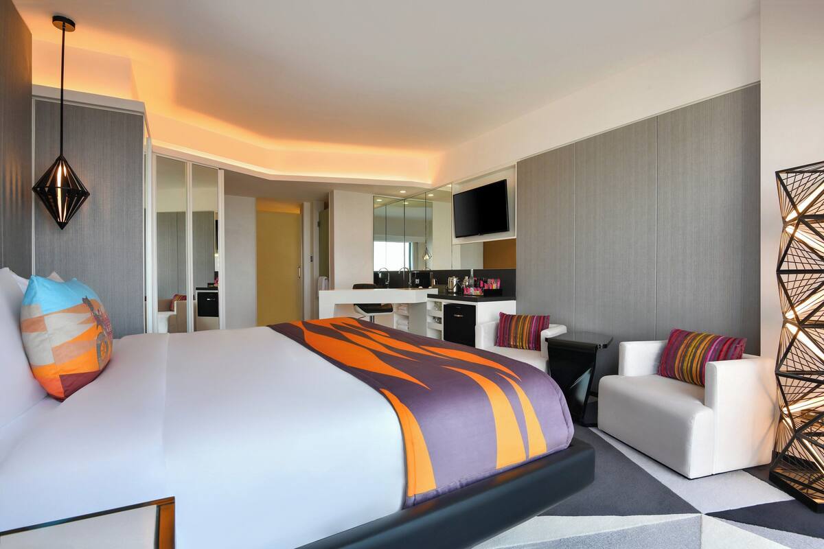 A modern hotel room with a large bed, a sofa, a desk, and a TV.