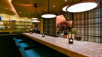 A bar area with a long counter, blue bar stools, and pendant lighting.