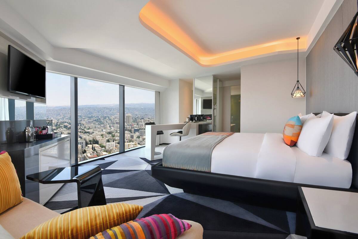 A modern hotel room with a large bed, a desk, a TV, and a city view.
