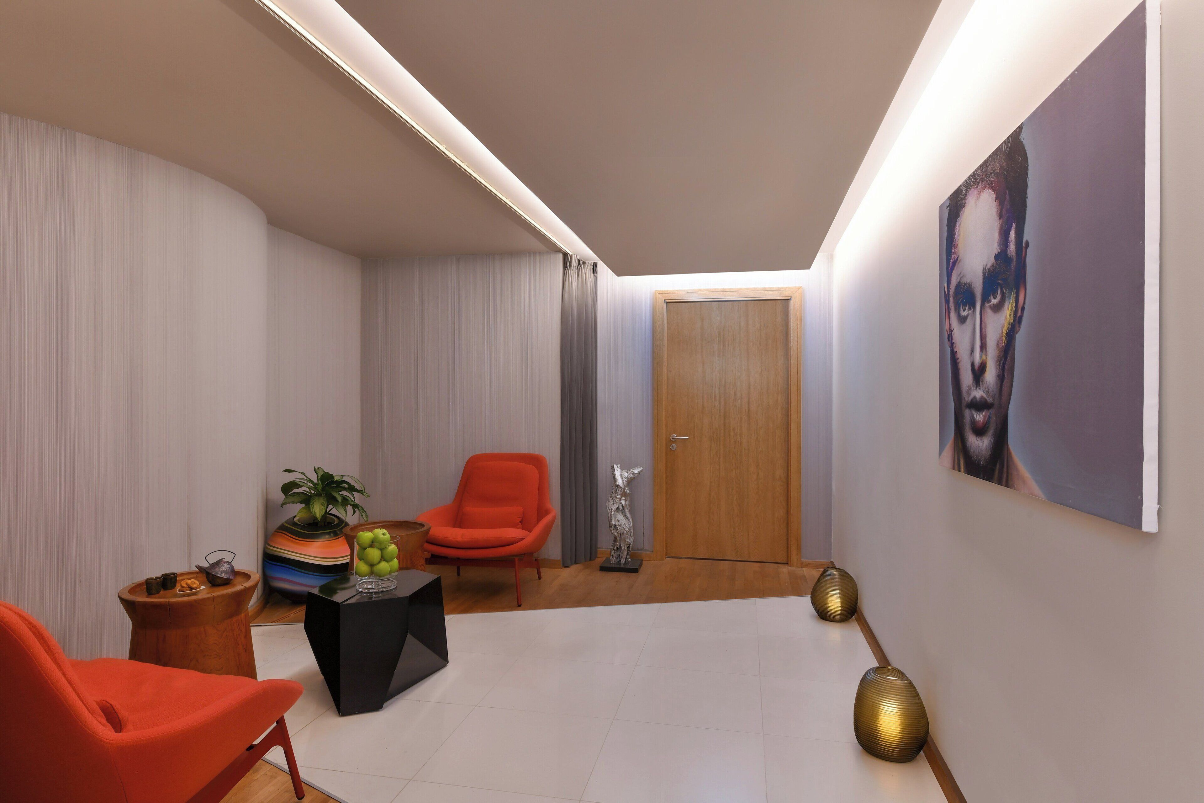Un salón moderno con una butaca roja, una mesita auxiliar negra y una puerta de madera.