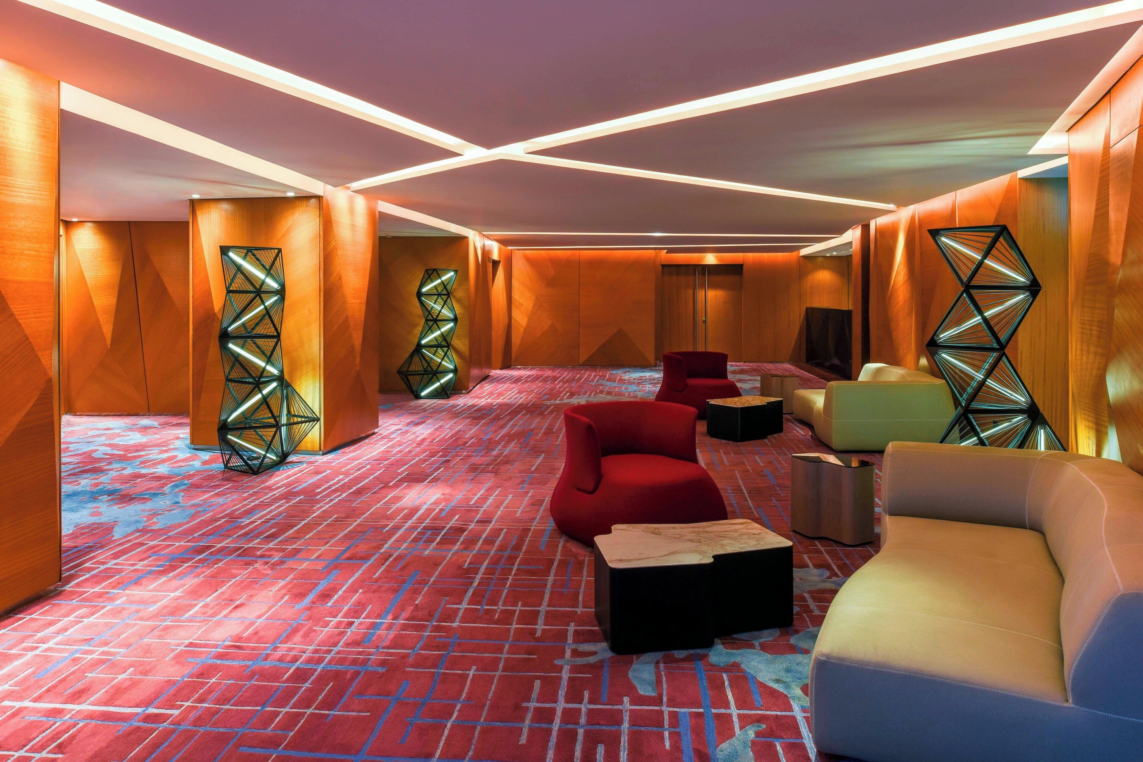 Un moderno vestíbulo de hotel con diseños geométricos en las paredes, asientos mullidos y una alfombra estampada.