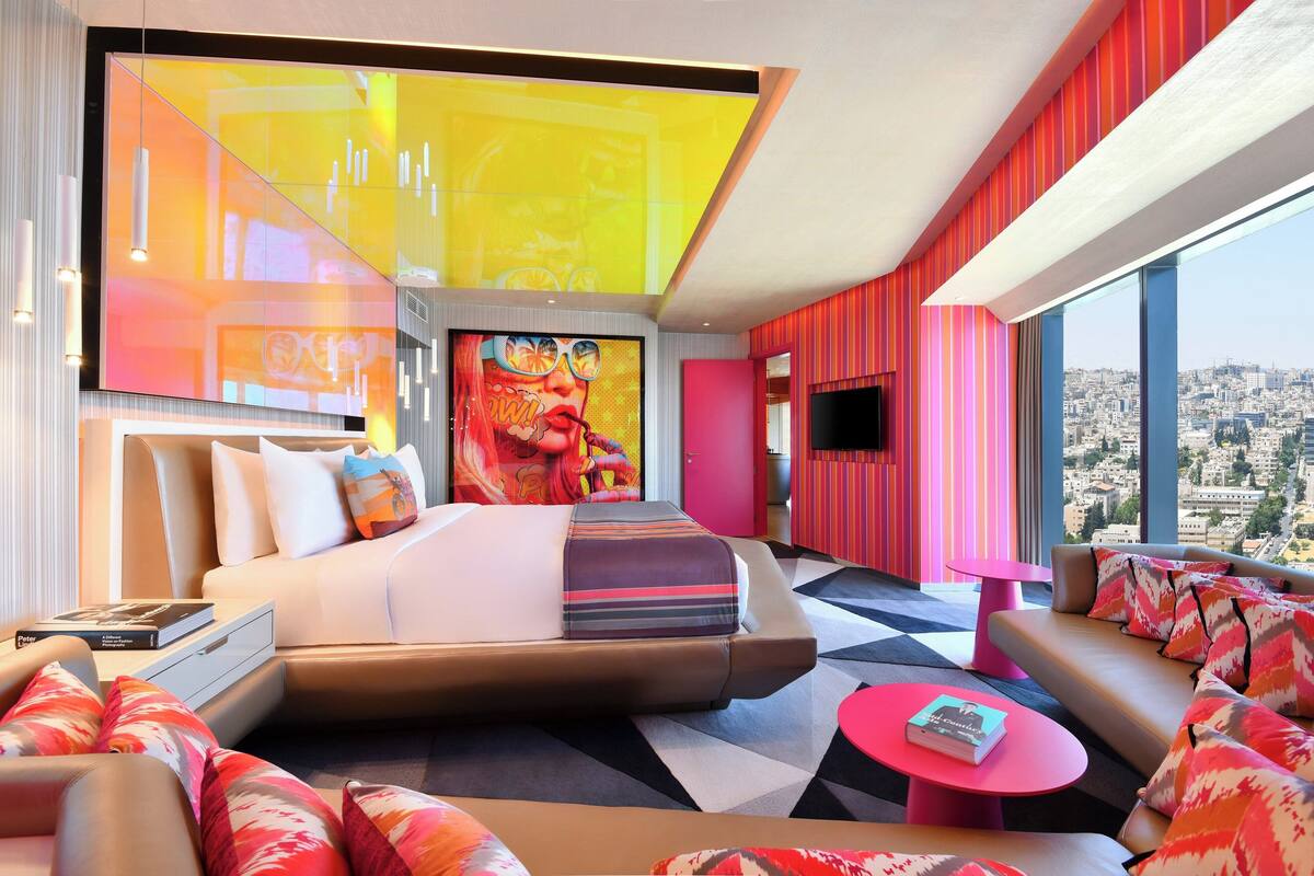 A modern hotel room with a large bed, a sofa, a coffee table, and a city view.