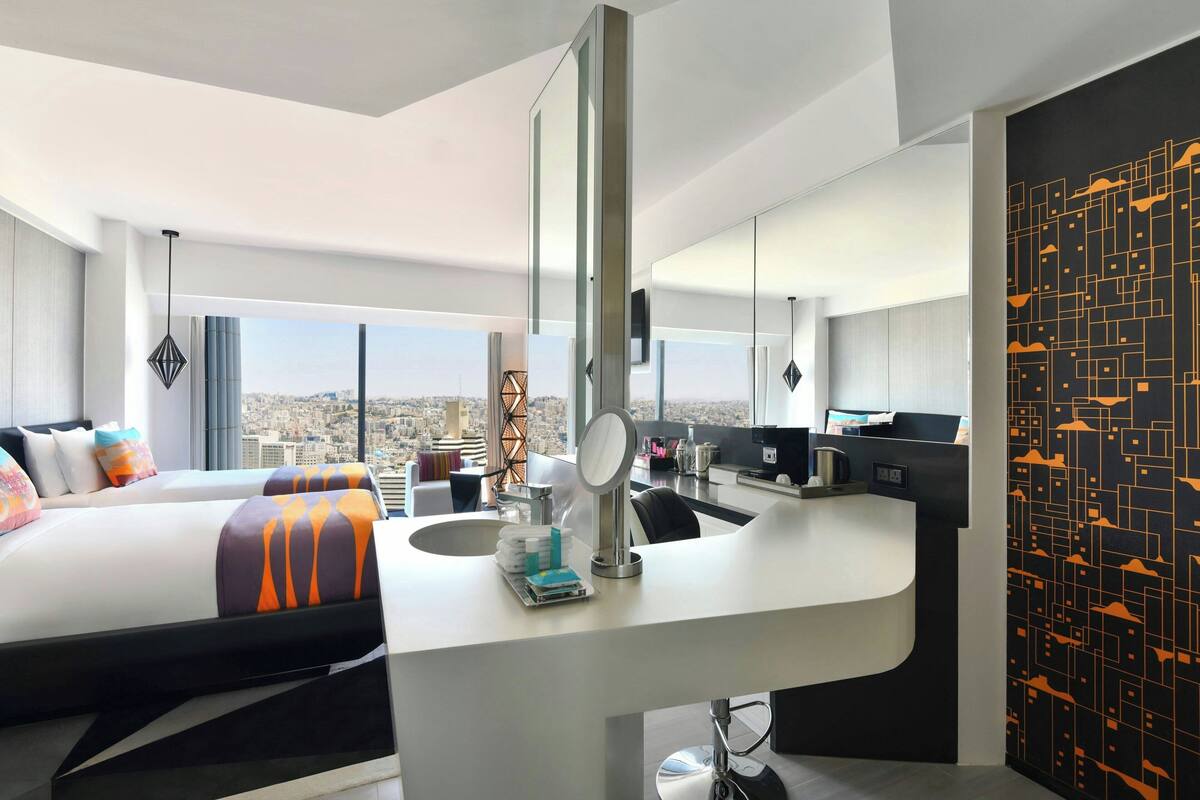 A modern hotel room with a large bed, a desk with a mirror, and a city view.