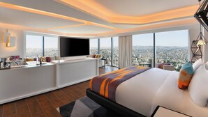 A modern hotel room with a large bed, a TV, a desk, and a view of the city. - W Amman (Amman)
