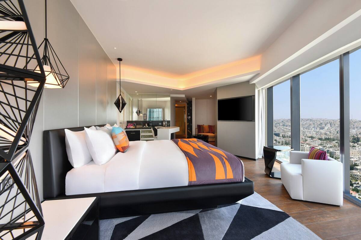 A modern hotel room with a large bed, a desk, a sofa, and a city view.