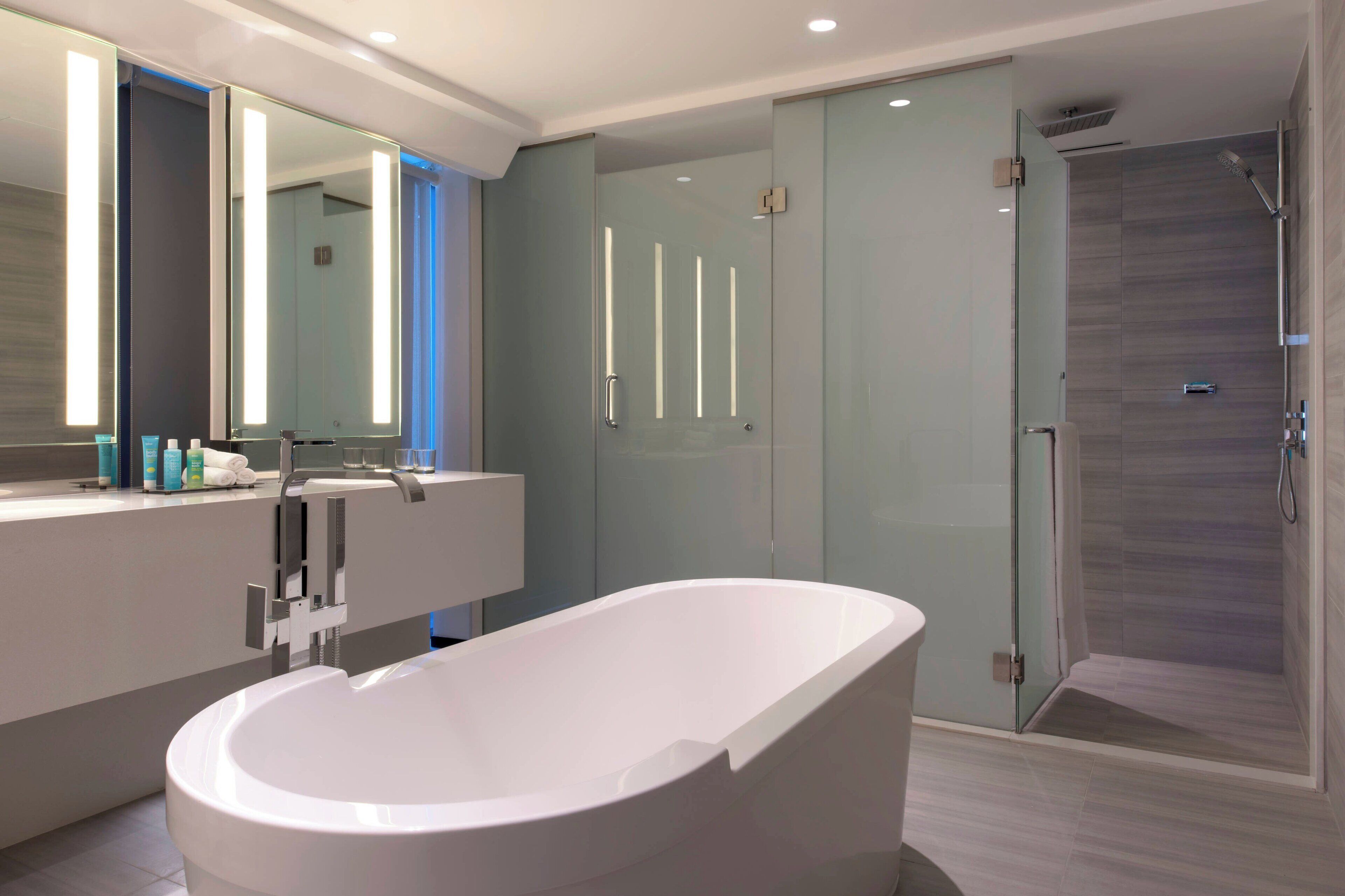 A modern bathroom with a freestanding bathtub, a glass-enclosed shower, and a large mirror with vertical light strips.