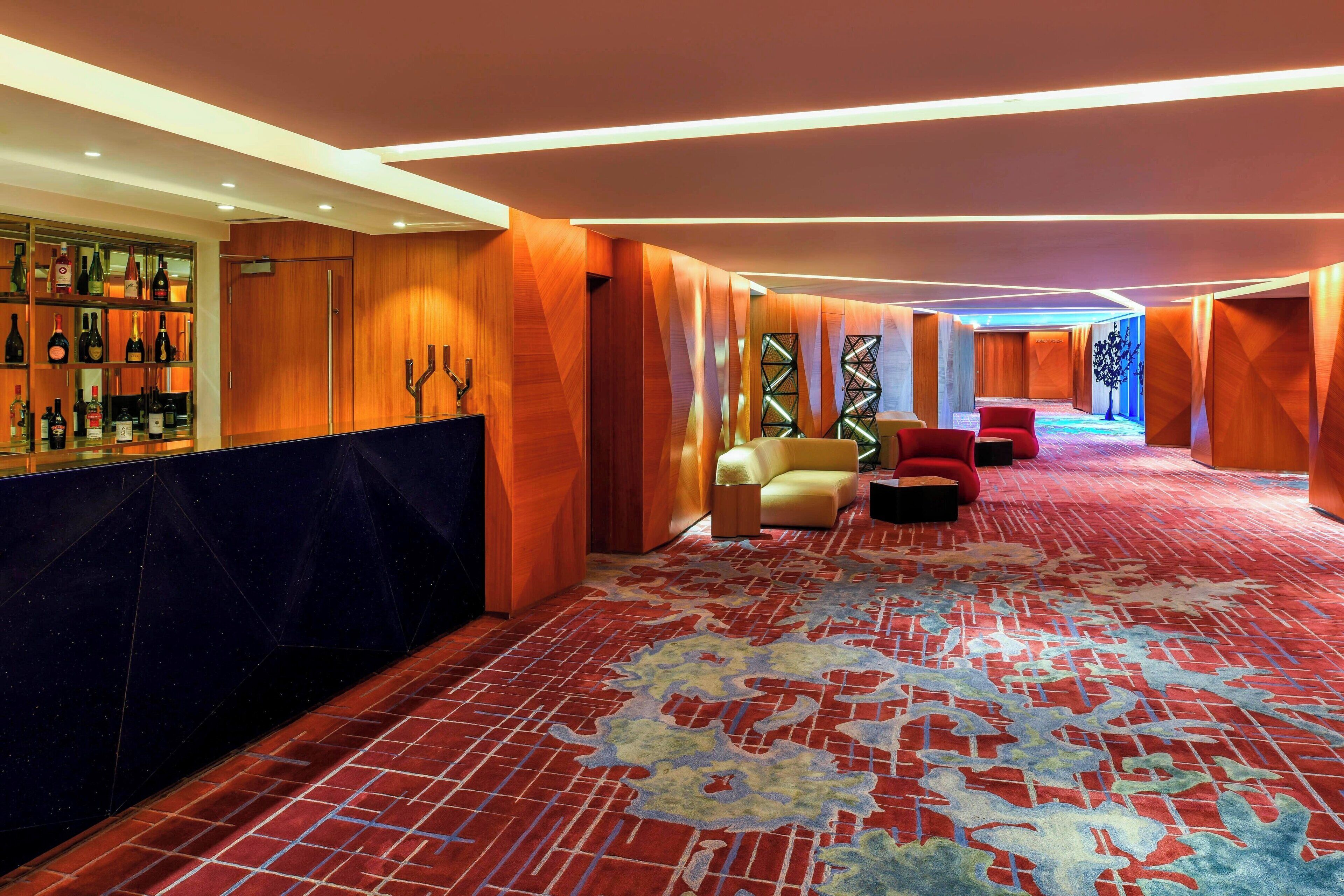 Un vestíbulo de hotel con alfombra roja, paneles de madera y una zona de bar con botellas de vino.
