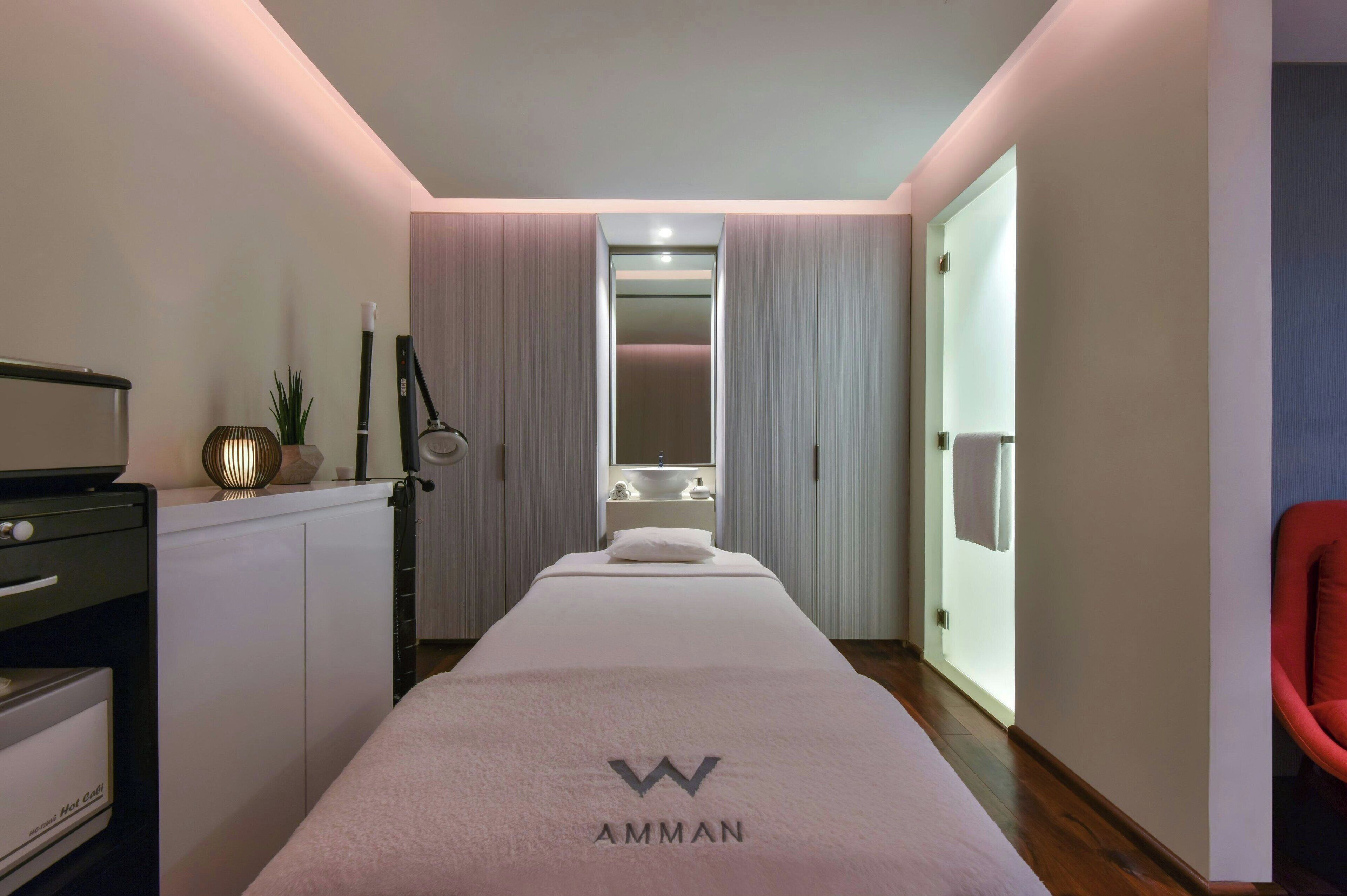 Une chambre d’hôtel moderne avec un grand lit, un bureau avec un ordinateur, une petite plante et une chaise rouge.
