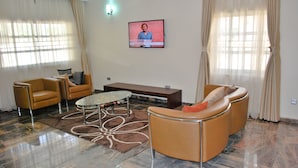 A living room with a sofa, armchairs, a coffee table, and a flat-screen TV mounted on the wall. - Chateau De Trybze (Abuja)