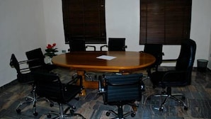 A conference room with a large oval table, black office chairs, and two windows with blinds. - Chateau De Trybze (Abuja)
