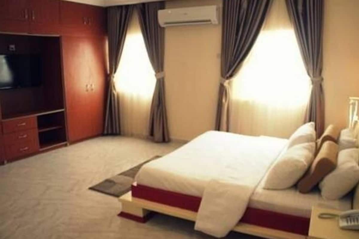 A hotel room with a bed, a TV, a wardrobe, and an air conditioning unit.