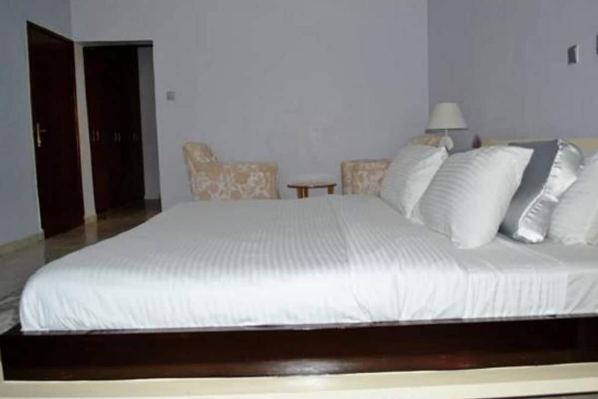 A bedroom with a large bed, two chairs, a small table, and a lamp.
