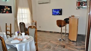 A dining area with a round table set for two, a bar area with a counter and stools, and a television mounted on the wall. - Chateau De Trybze (Abuja)