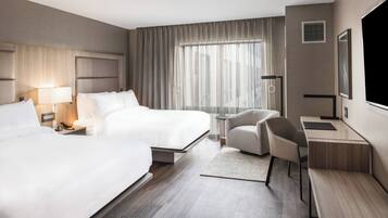 Une chambre d’hôtel avec deux lits, un bureau, une chaise, une télévision et une grande fenêtre avec des rideaux.
