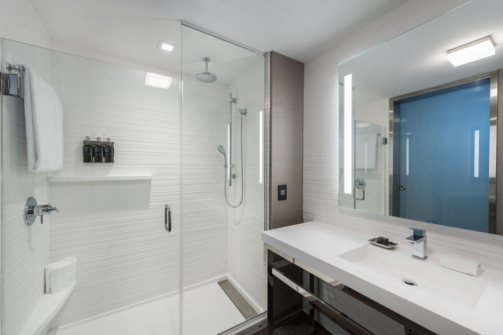 Une salle de bain moderne avec une douche à parois de verre, un lavabo blanc avec un miroir et une porte bleue.