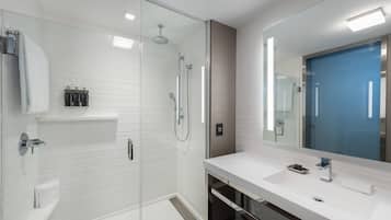 Une salle de bain moderne avec une douche à parois de verre, un lavabo blanc avec un miroir et une porte bleue.