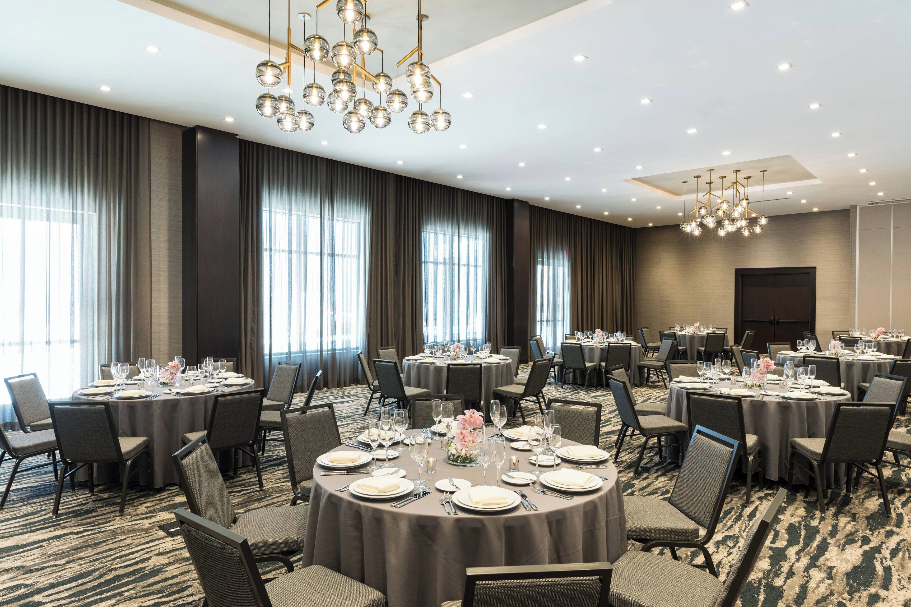 Un salón de conferencias con varias mesas redondas dispuestas para una comida, equipado con sillas y cubiertos.