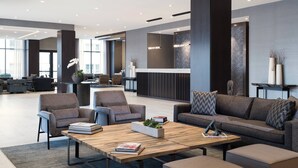 A modern lobby with a reception desk, seating area with sofas and armchairs, and a large window providing natural light.