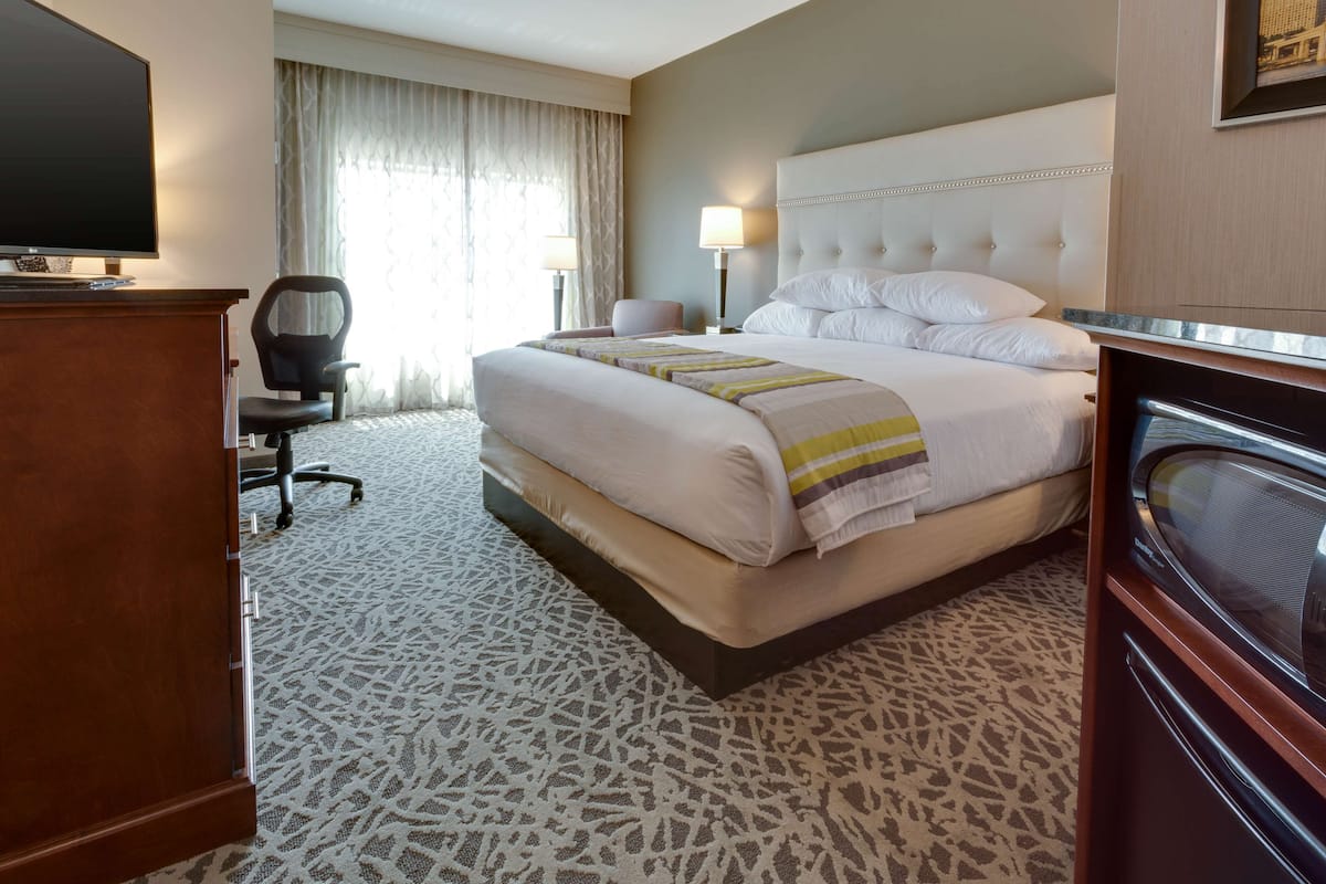 A hotel room with a large bed, a television, a desk with a chair, and a window with curtains.