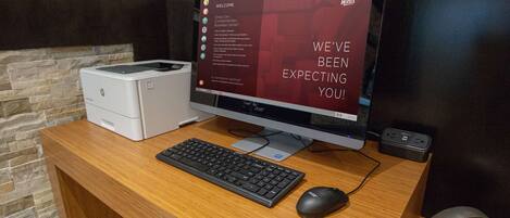 A reception desk with a computer monitor displaying a welcome message, a printer, a keyboard, a mouse, and a small speaker.