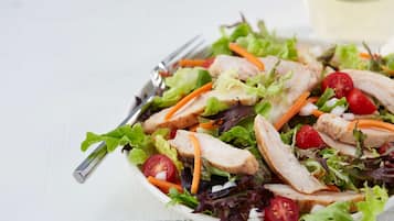 A plate of salad with lettuce, tomatoes, carrots, and chicken slices.