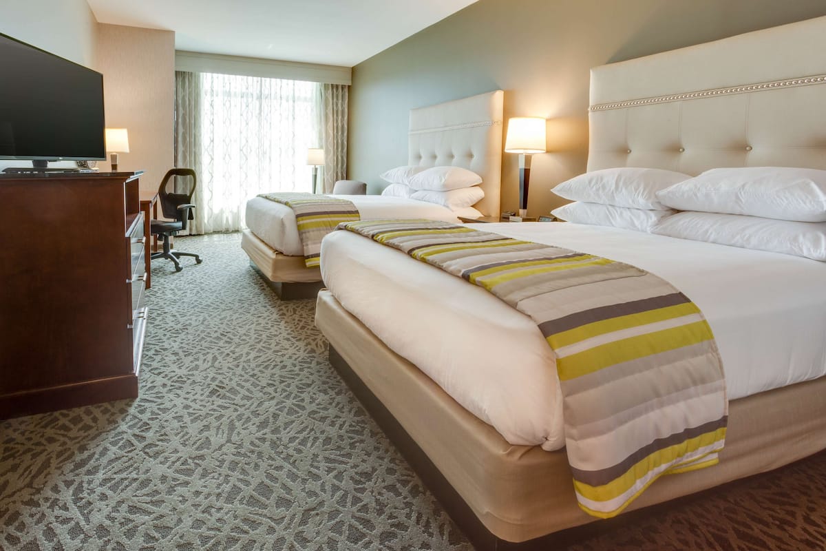 A hotel room with two beds, a TV, a desk, and a chair.