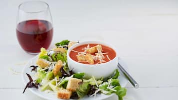 A white plate with a salad and a bowl of tomato soup garnished with croutons and cheese.