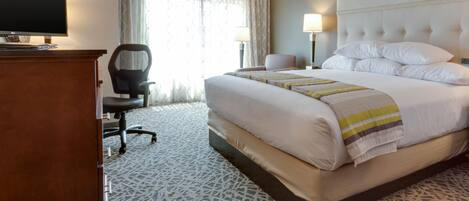 Habitación de hotel con una cama grande, un escritorio con televisor, una silla y una lámpara.