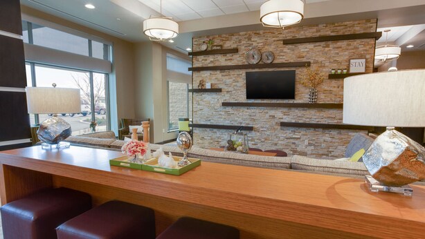 A modern bar area with a stone wall, flat-screen TV, and bar stools. - Drury Inn & Suites Pittsburgh Airport Settlers Ridge (Pittsburgh)
