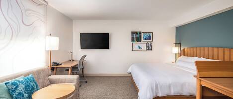 Una habitación de hotel con cama, escritorio, sillón, sofá y televisor en la pared.