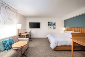 A hotel room with a bed, a desk, a chair, a sofa, and a TV on the wall.