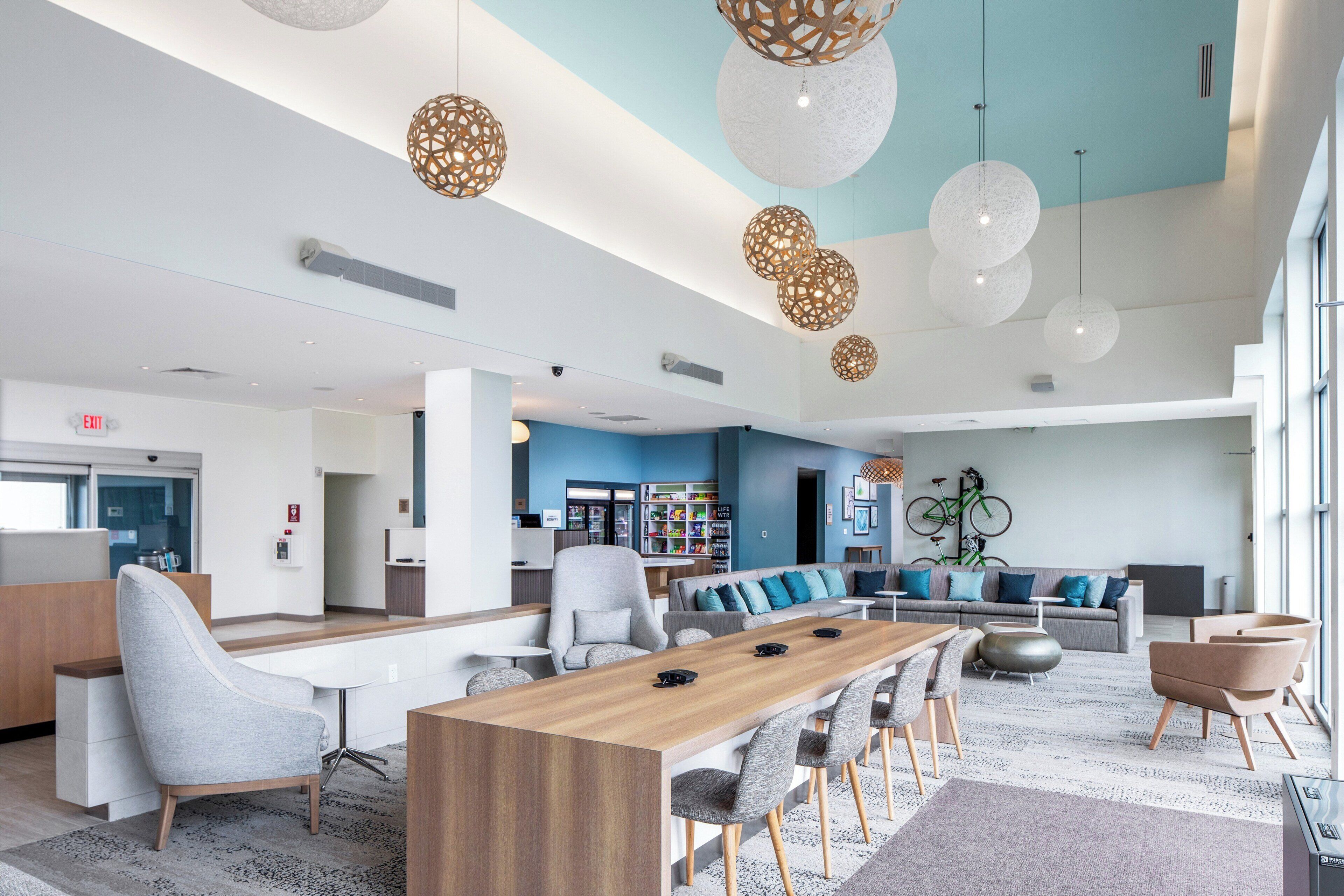 A spacious lobby with a long wooden reception desk, comfortable seating, and modern pendant lighting.