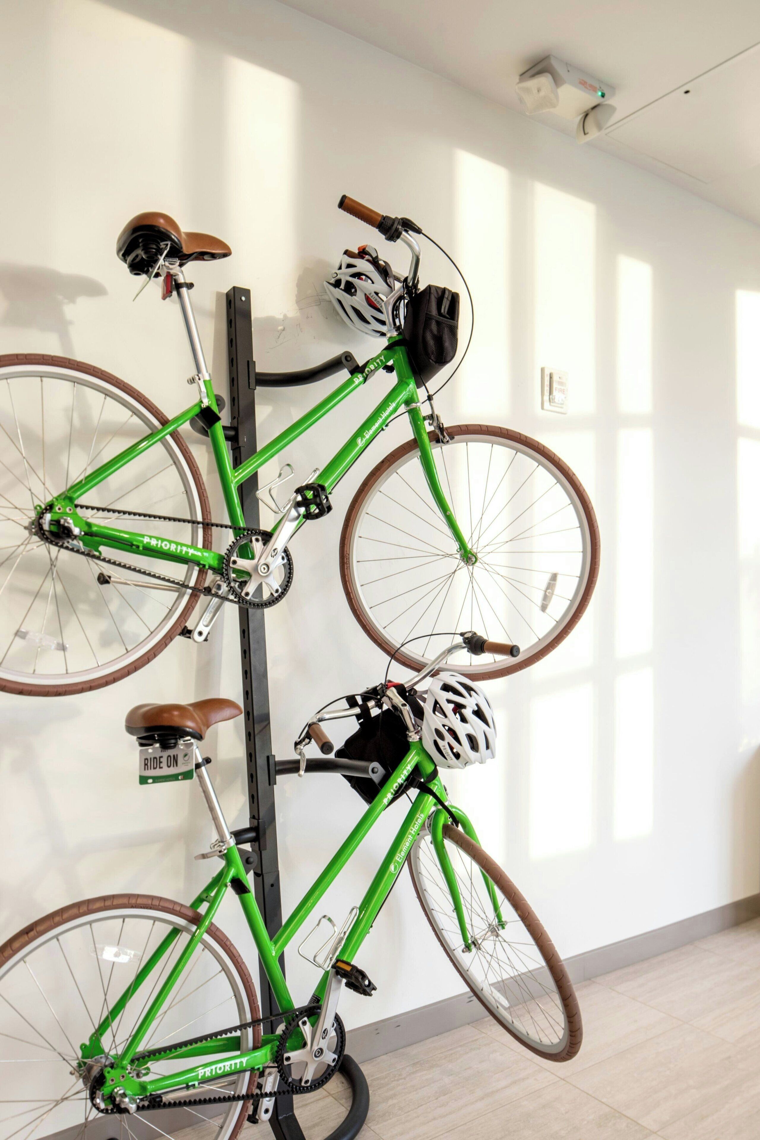 A green bicycle with brown seats and a helmet hanging on a wall-mounted rack.