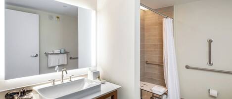 A bathroom with a large mirror, a sink, a bathtub, and a shower.