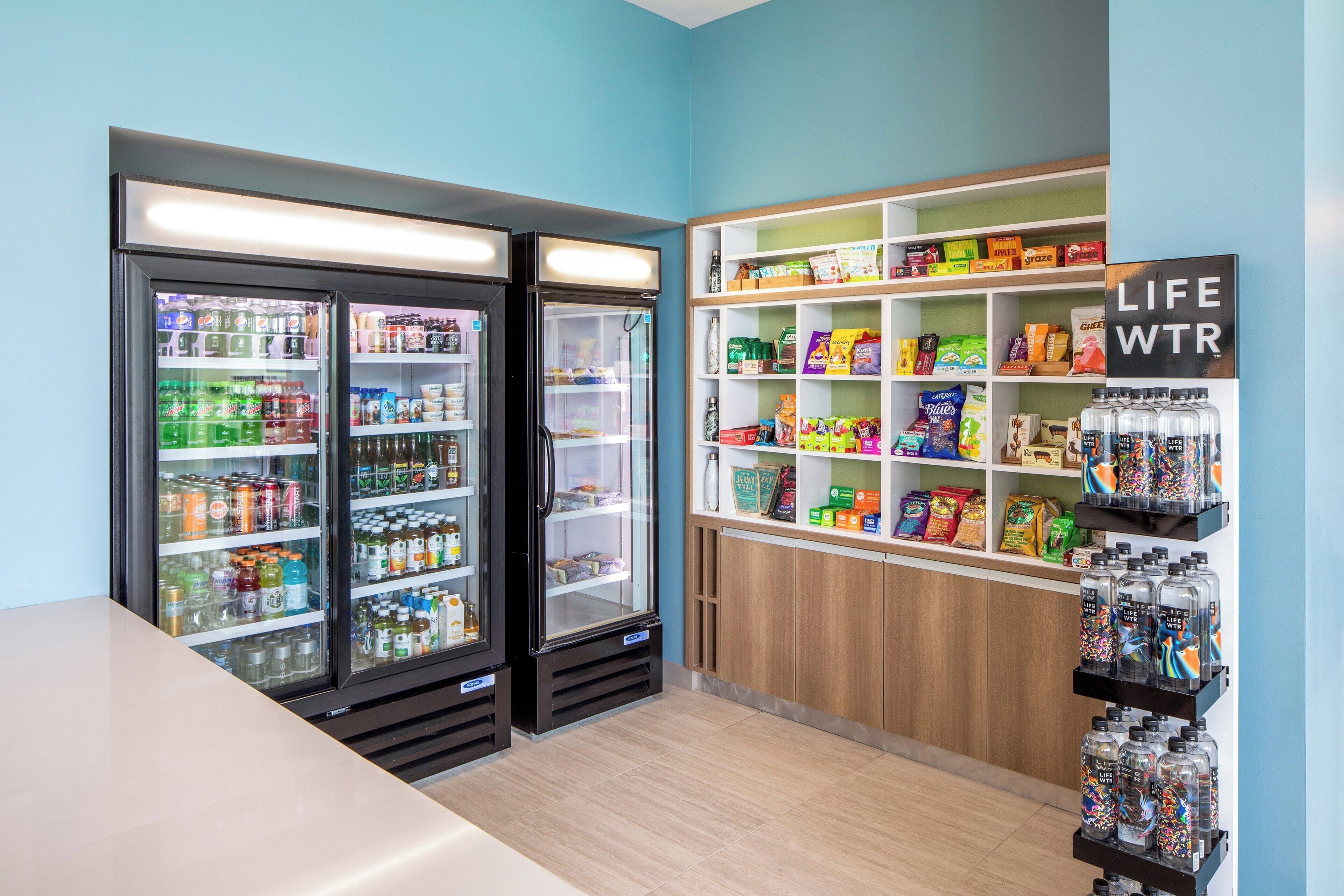 A room with two refrigerators stocked with beverages, shelves with snacks and drinks, and a sign that reads 'LIFE WTR'.