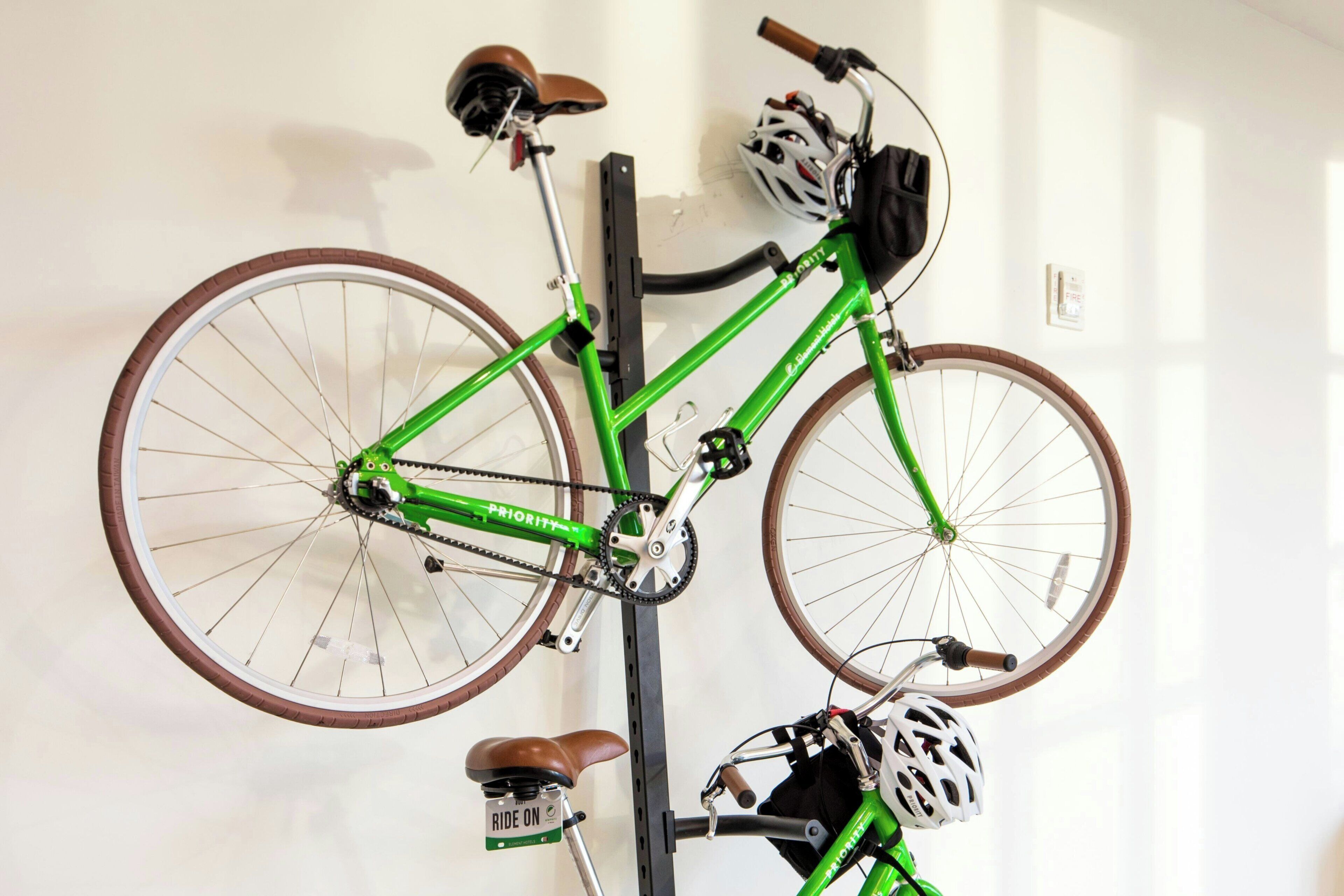 A green bicycle with a brown seat and a helmet hanging on the wall.