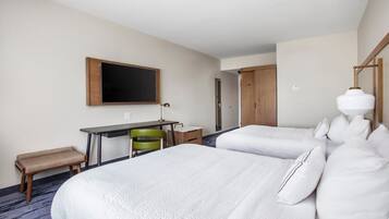 Habitación de hotel con dos camas, un escritorio con una silla, un televisor y un banco.