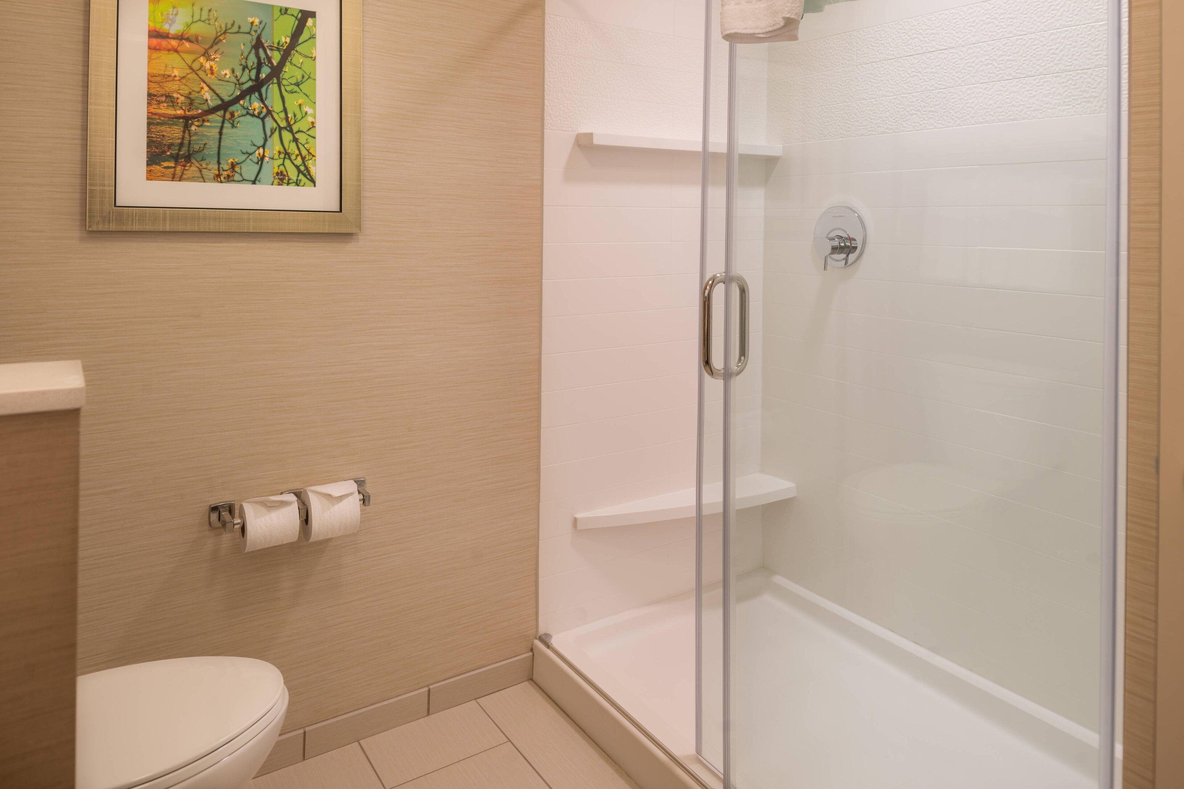 A bathroom with a toilet, a glass-enclosed shower, and a framed picture on the wall.