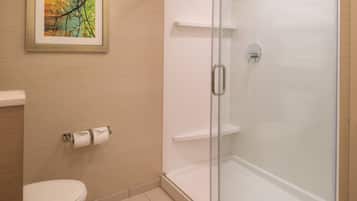 A bathroom with a toilet, a glass-enclosed shower, and a framed picture on the wall.