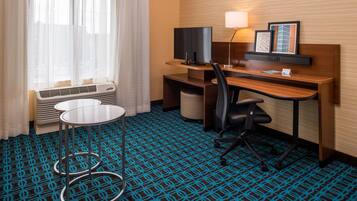 A hotel room with a desk, chair, TV, lamp, and a patterned carpet.