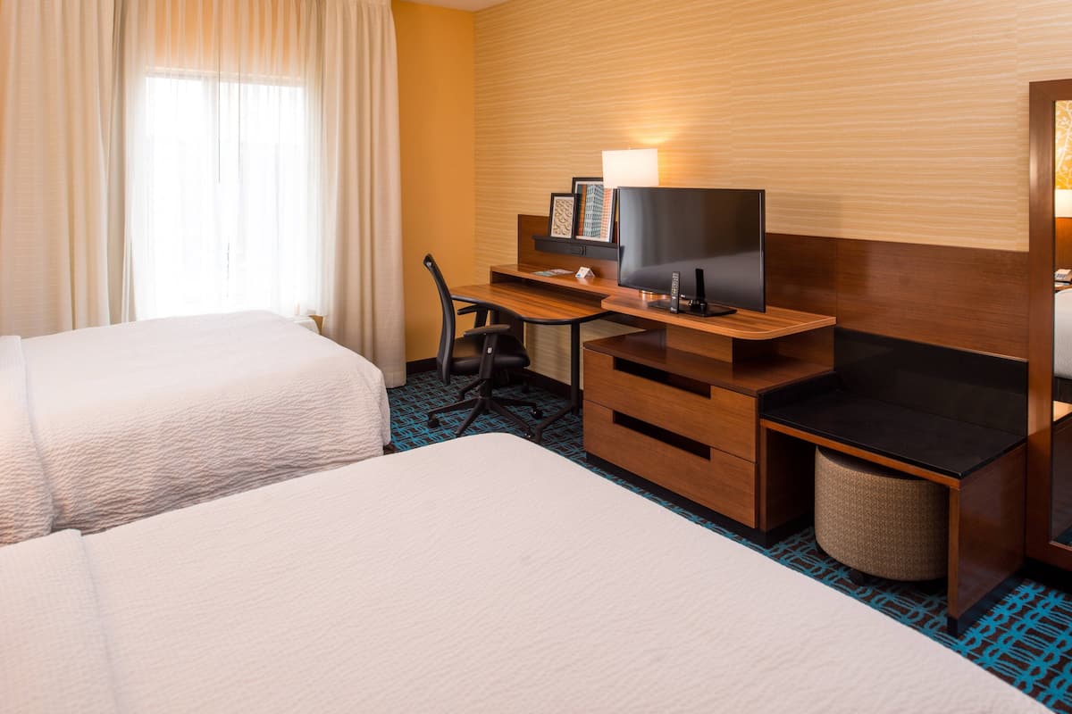 A hotel room with two beds, a desk with a TV, and a chair.