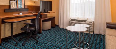 Habitación de hotel con escritorio, silla, televisor, lámpara y una pequeña mesa redonda.