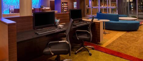 Un hall de hotel con recepción, estaciones de computadoras, una tienda de conveniencia y un área de estar.
