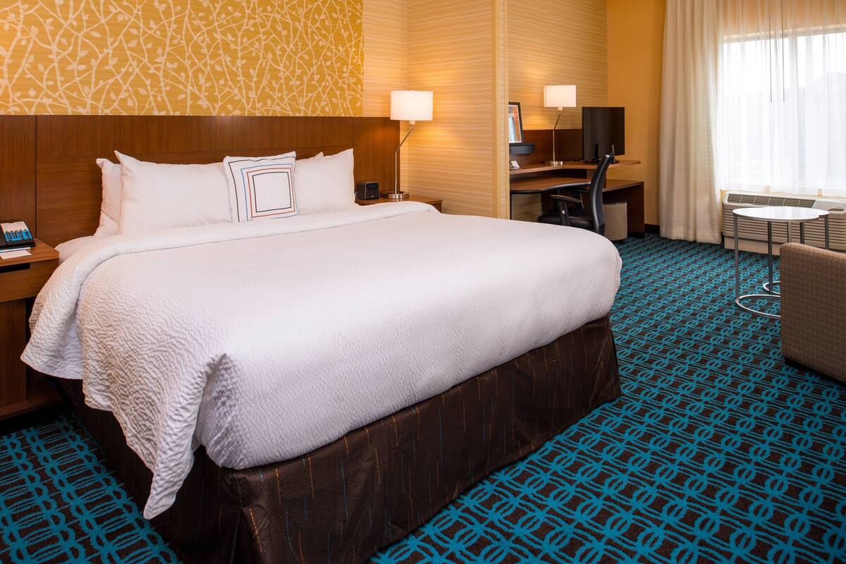 A hotel room with a large bed, a desk, a chair, and a TV.