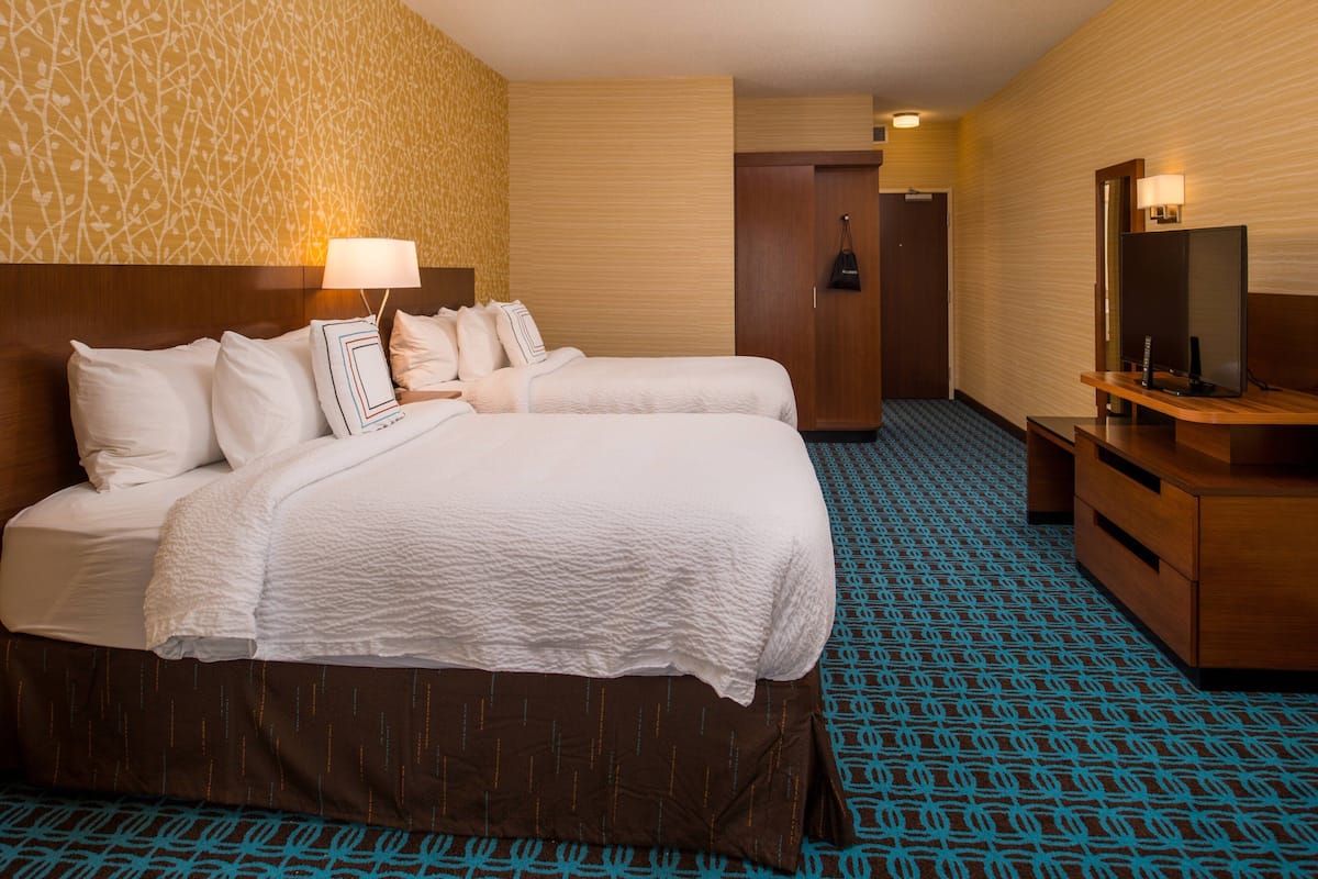 A hotel room with two beds, a desk, a TV, and a wardrobe.