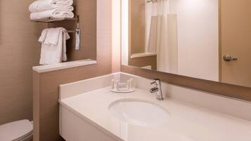 Un baño con un lavabo blanco, un espejo, un toallero con toallas dobladas y una cortina de ducha.